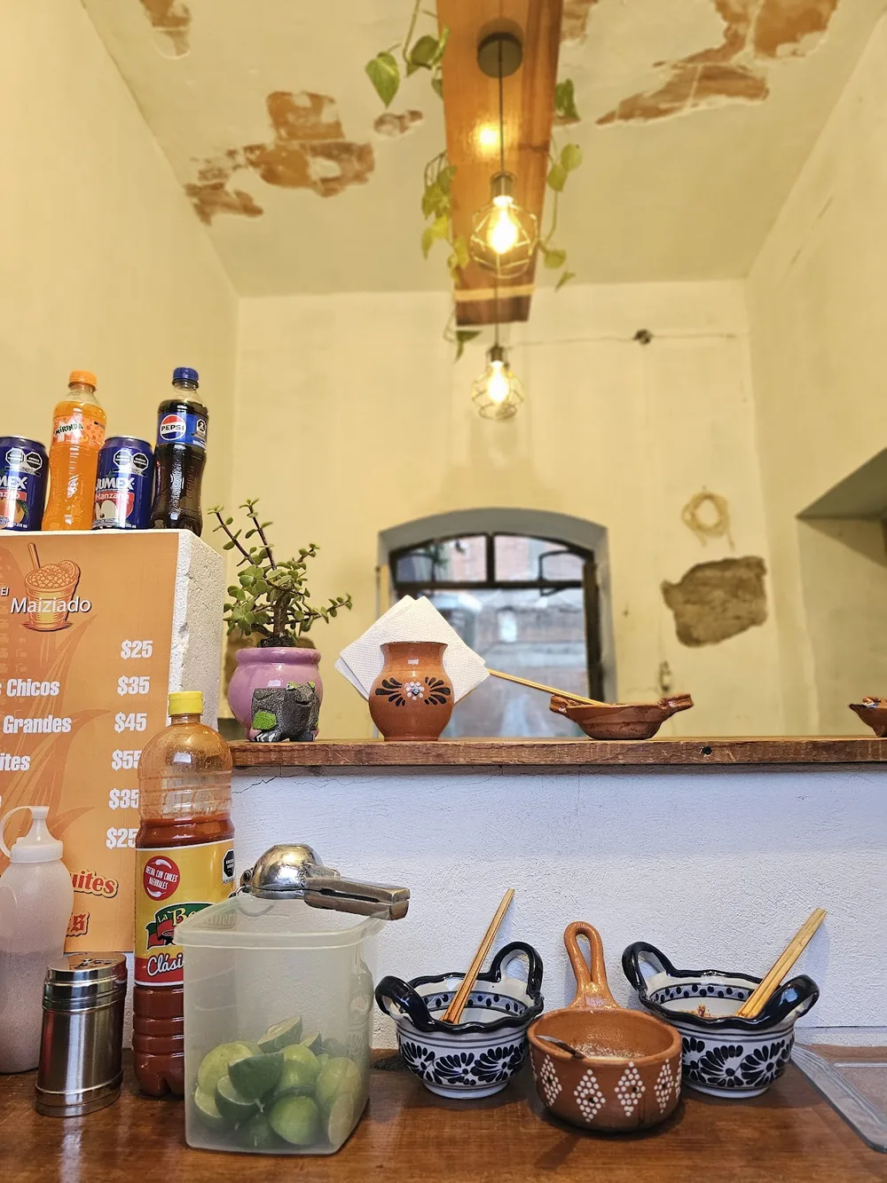 La barra del local: refrescos, cazuelitas de talavera, limones y el letrero de precios